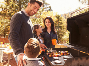 Family enjoying a barbecue outside in sunlight.
